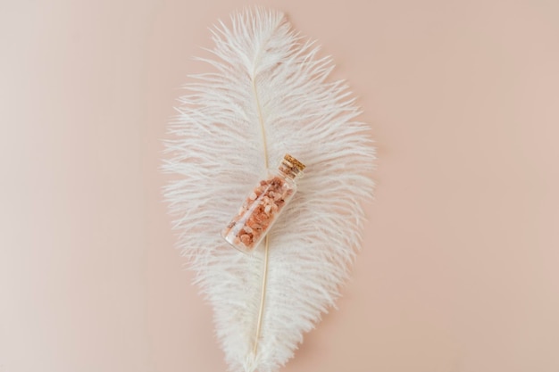 A pink sea salt in a small glass bottle lying on a white feather