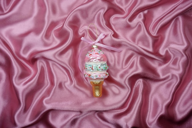 On a pink silk background is a Christmas tree toy in the form of ice cream