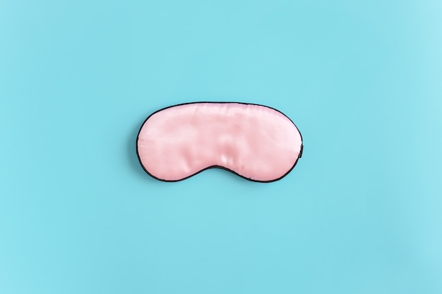 Pink silk sleep mask for eyes on a blue background. Top view Flat lay Copy space. Concept eye protection from light for good sleep