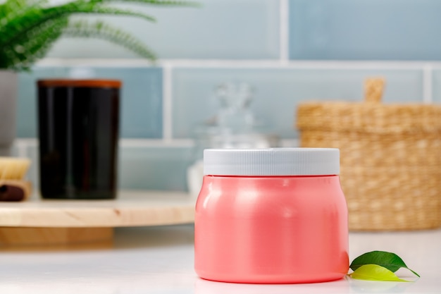 Pink skincare product jar against blue background, front view