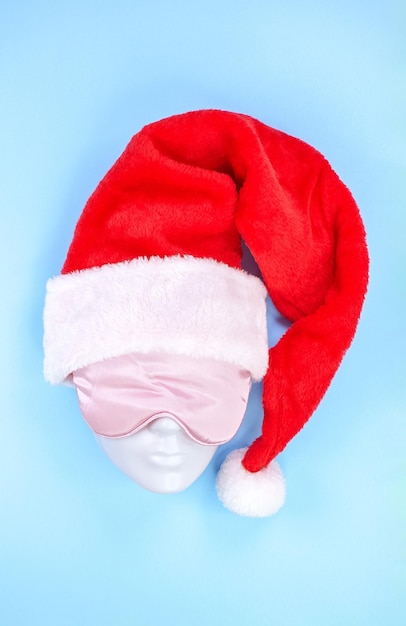 Pink sleeping eye mask on mannequin face with red christmas hat on blue background