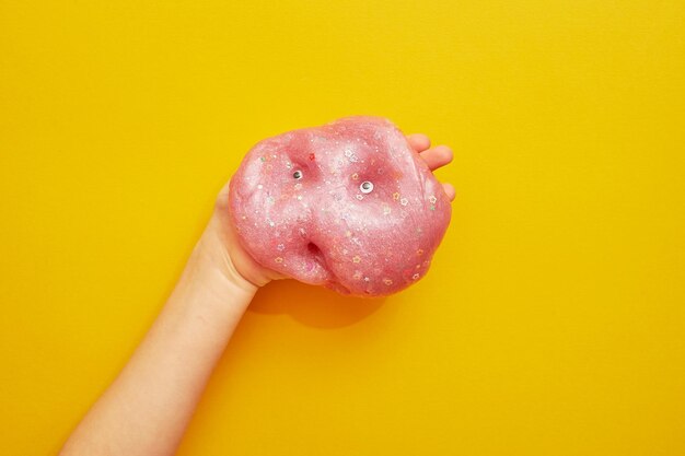 Pink slime with sequins on a yellow background in a child's handWith eyes Creativity