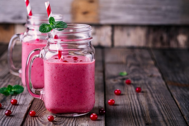 Pink smoothie with wild cranberries in mason jar with mint and straw on rustic wooden background