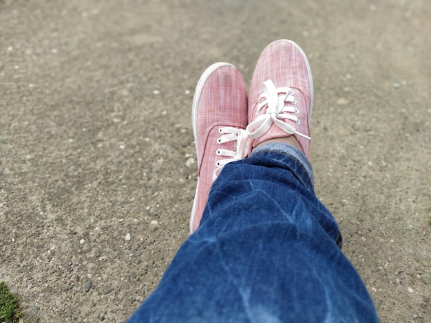 Pink sneakers with white laces on the legs blue jeans wrapped underneath view from above carefree