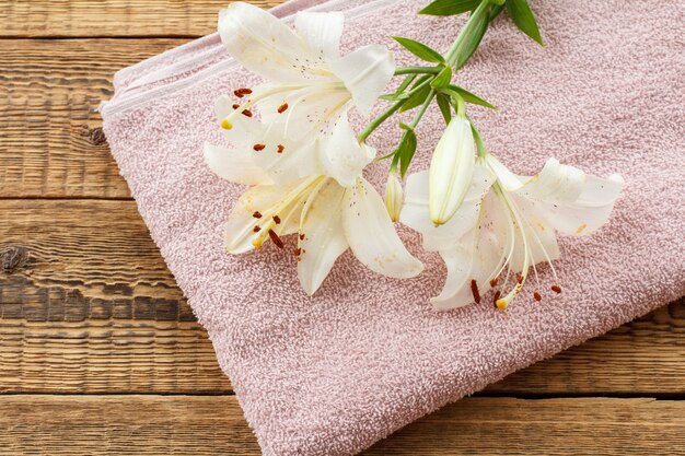 Pink soft terry towel with bouquet of white lily flowers on old wooden boards. Top view.