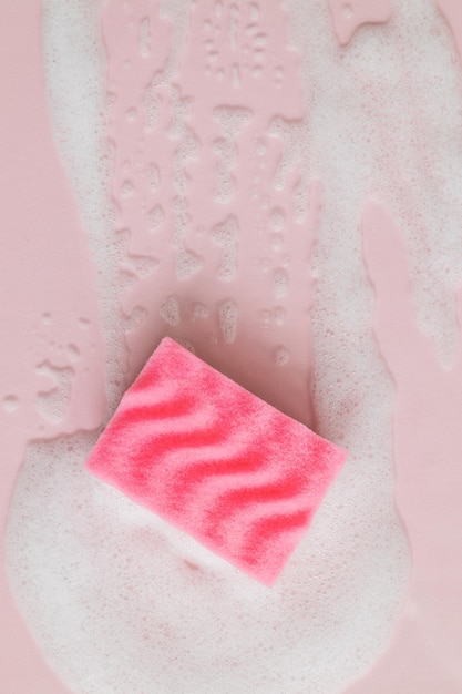 ピンクの背景に洗剤の泡とピンクのスポンジは、クリーニングの概念をクローズアップ