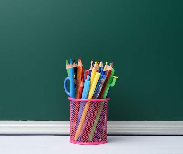 Pink stationery glass with multi-colored wooden pencils and pens, chalkboard background, copy space