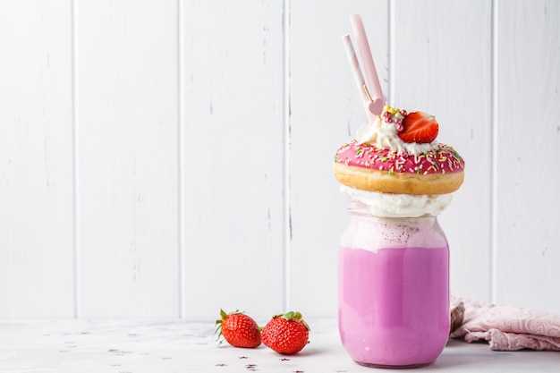 Pink strawberry Freak Shake cocktail with donut and sweets on a white background