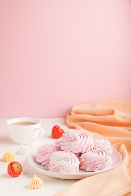 Pink strawberry homemade zephyr or marshmallow with cup of coffee on white surface. side view, selective focus, copy space.