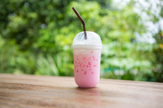 Pink strawberry milk pink ice drink in plastic cup juice for summer and straw on wooden table with nature 