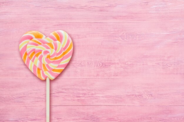 Pink striped heart-shaped lollipop on pink wooden background copy space.