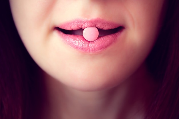 Pink tablet in the mouth of the woman