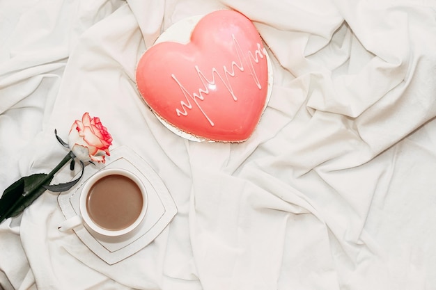 Pink tea rose with heart shaped pink mousse cake with a cup of coffee