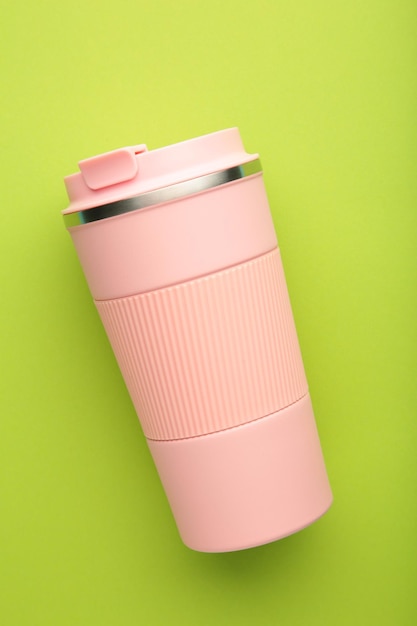 Pink thermo cup or thermos mug for tea or coffee on green background Hot beverage