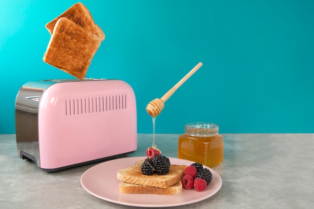 튀긴 빵 조각이 튀는 핑크 토스터기. 꿀, 딸기와 함께 아침 식사