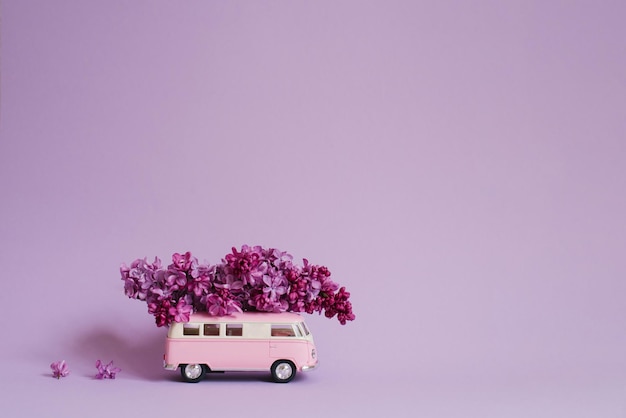 Pink toy car bus with lilac flowers on the roof on a lilac background flower delivery birthday