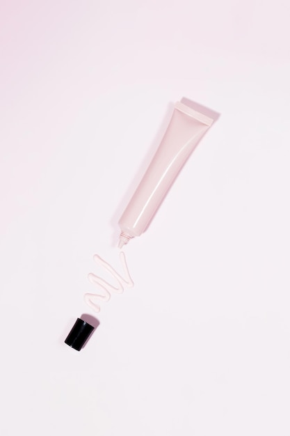 A pink tube with cosmetics and a squeezed creamy cosmetic product on a pink background Face cream foundation