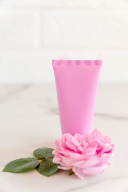 Pink tube with rose face or body cream or scrub decorated with pink core flowers. Skin care concept. Unbranding mockup.