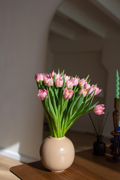 木製のテーブル上のベージュ色の花瓶にピンクのチューリップ