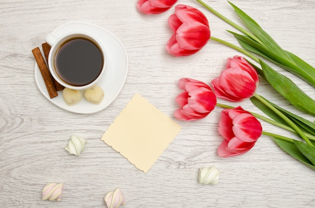 Pink tulips, blank sheet of paper, mug of coffee and marshmallows
