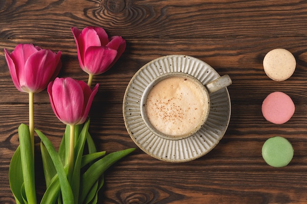 Pink tulips, cup with coffee and macaroon cookies on a wooden table, copy space