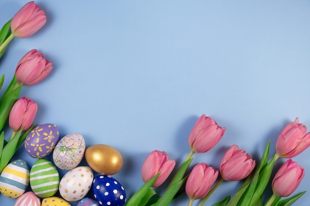 Pink tulips flowers and colourful eggs isolated on blue