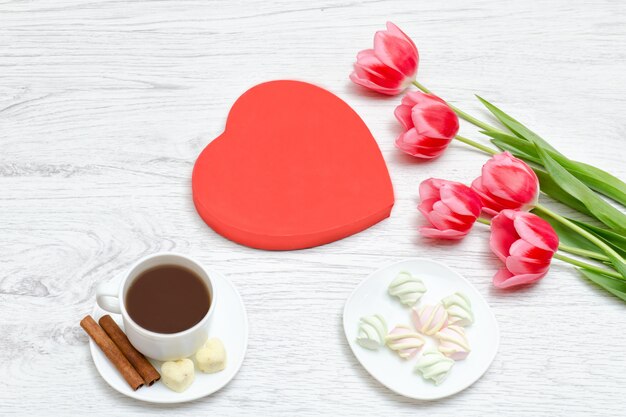 Pink tulips, mug of coffee and marshmallow. Red heart shaped gift box