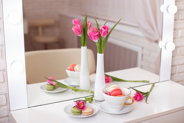 Pink tulips in vase, cup and macaroons on table in beauty salon