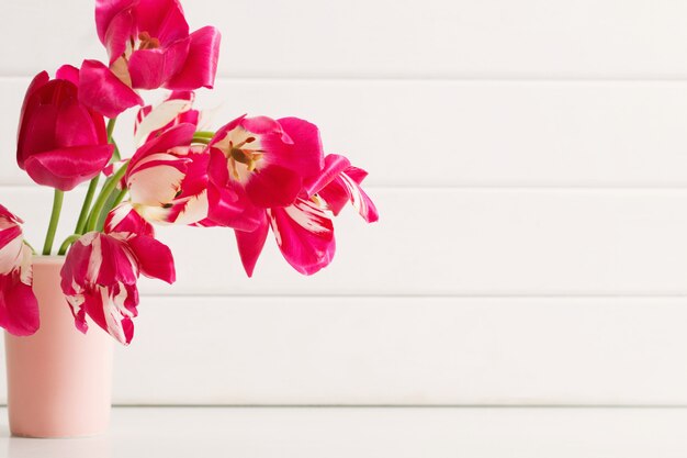 Pink tulips in vase on white wooden background