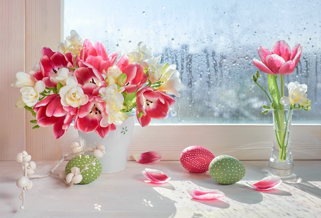 Pink tulips and white freesia flowers with Easter decorations on the window board