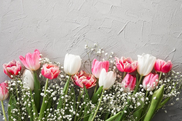 Pink tulips and white gypsophila flowers bouquet on a stylish gray stone background Mothers Day birthday celebration concept Copy space for text