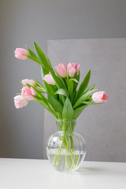 Pink tulips with green leaves in a glass vase