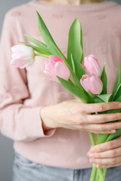 彼女の手でチューリップを保持しているガラスのvasea女性の緑の葉とピンクのチューリップfloristfloristry