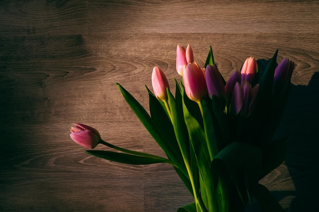 Pink tulips on a wooden background closeup Sun rays