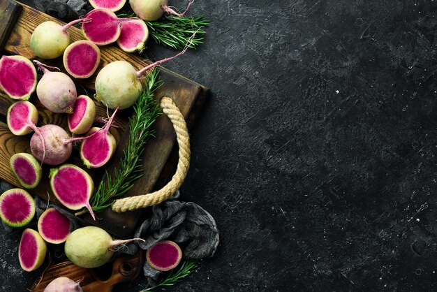 Pink watermelon radish lying on a couple of whole light green watermelon radishes On a black stone background