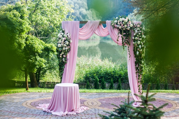 夏の外の花白とピンクの装飾が施されたピンクのウェディングアーチ