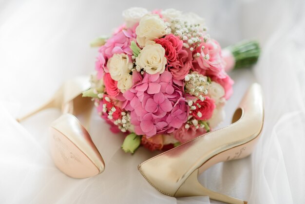 Pink wedding bouquet lies between golden shoes