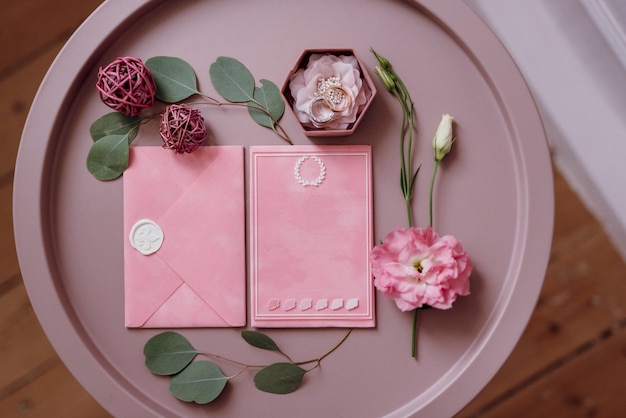 Pink wedding invitation in a gray envelope on a table with green sprigs