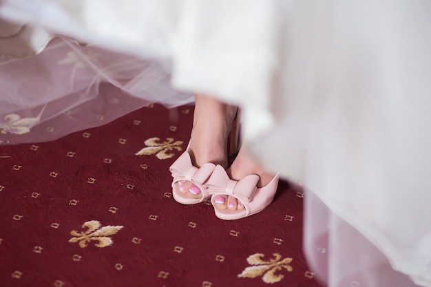 Pink Wedding shoes with bow on the feet of the bride in the white dress close up