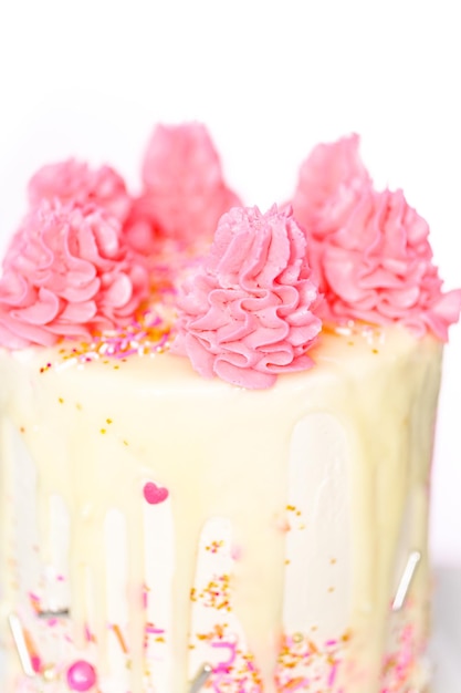 Pink and white buttercream cream cake with pink sprinkles and white chocolate ganache drip.