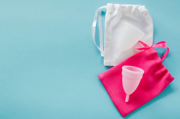 Pink and white menstrual cups with bags on blue background