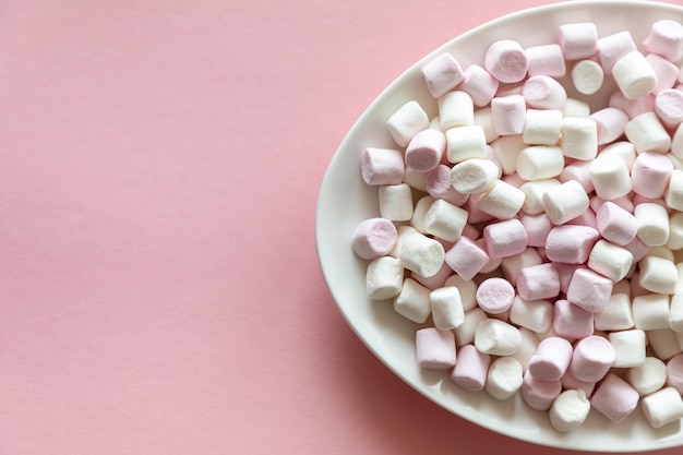 Pink and white mini marshmallows in white plate on pink background with free space for text