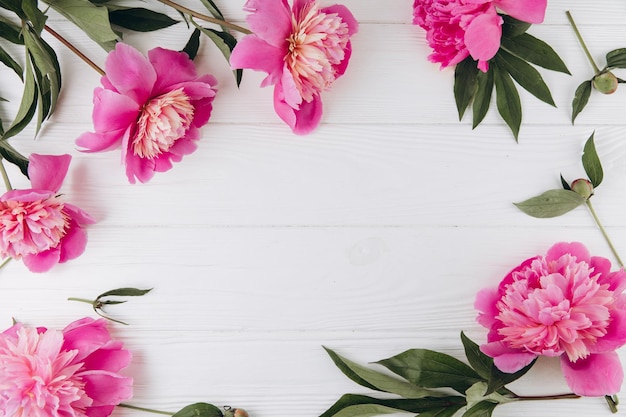 Розовые и белые пионы на белом деревянном фоне копируют пространство плоской поздравительной открытки