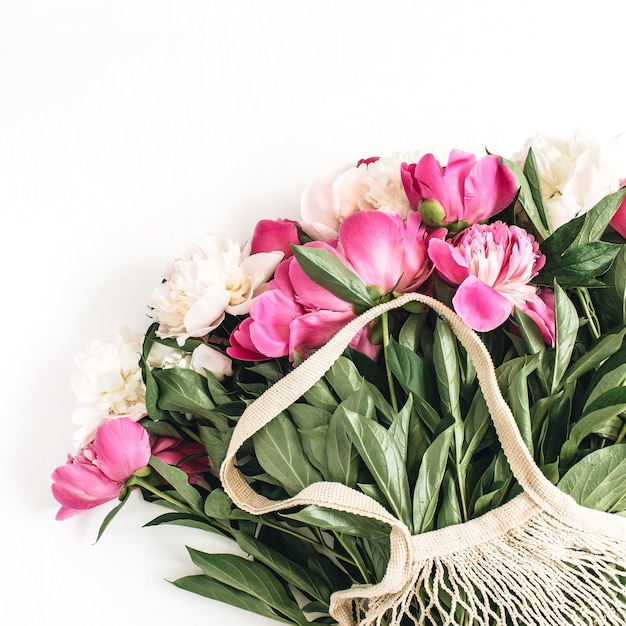 Fiori di peonia rosa e bianchi in sacchetto di stringa sulla superficie bianca