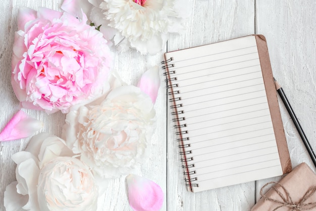 Pink and white peony flowers with blank lined notebook and gift box on white wooden table