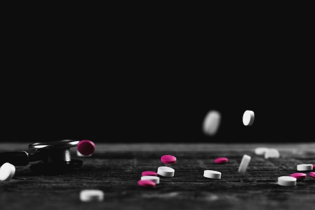 Розовые и белые таблетки летают сыпятся на деревянный стол на черном фоне
