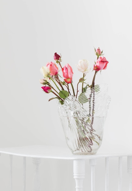 Pink and white roses on glass vase on white wooden shelf