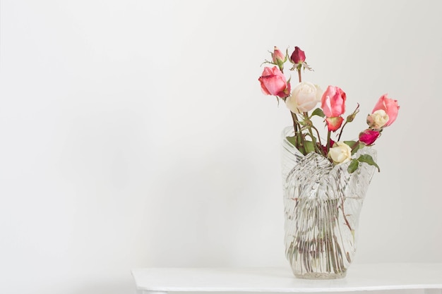 Pink and white roses on glass vase on white wooden shelf