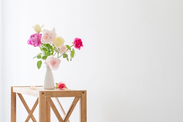 Pink and white roses in white ceramic vase on white background