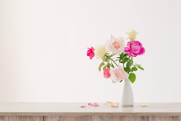 Pink and white roses in white ceramic vase on white background